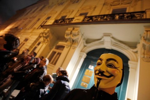 A man wearing an anonymous mask stands in front of the Hungarian embassy in Vienna