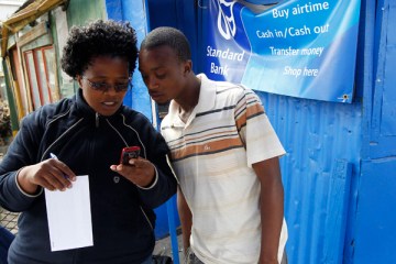 image: Staff from South Africa's Standard Bank show a newly signed client how to use mobile phone banking as part of a drive to take banking to poorer areas in Cape Town's Khayelitsha township, June 28, 2011.
